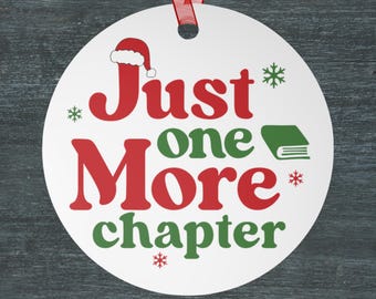 May include: A white, round Christmas ornament with the text "Just one More chapter" in red and green. A Santa hat and snowflakes are included in the design. A red ribbon is attached for hanging.
