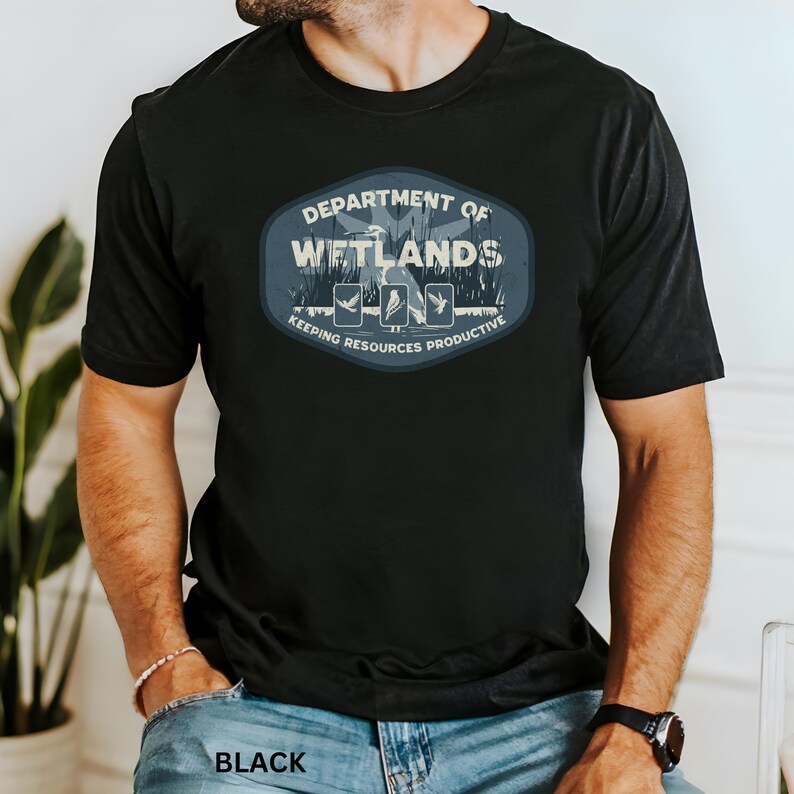 May include: Black t-shirt with a blue and white graphic that reads "DEPARTMENT OF WETLANDS" with illustrations of birds and the text "KEEPING RESOURCES PRODUCTIVE". The word "BLACK" is printed at the bottom of the shirt.