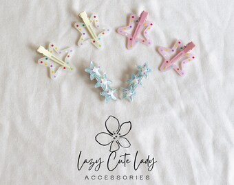 Puede incluir: Varias pinzas para el pelo en forma de estrella en colores pastel, rosa, amarillo y azul, algunas con lunares. La imagen también muestra un grupo de pinzas azules en forma de estrella y el texto "Lazy Cute Lady ACCESSORIES".