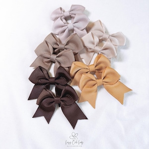 May include: Set of six brown, beige, and tan hair bows. The bows are made of grosgrain ribbon and are arranged in a fan shape.