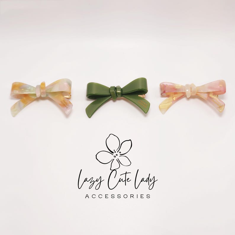 Pu&ograve; includere: Tre fermagli per capelli a forma di fiocco. Due fermagli presentano un motivo marmorizzato nei toni del giallo, rosa e bianco. Il terzo fermaglio &egrave; verde oliva. I fermagli sono su sfondo bianco. Il testo "Lazy Cute Lady ACCESSORIES" &egrave; sotto.