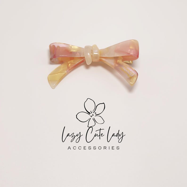 Pu&ograve; includere: Fermaglio per capelli a forma di fiocco nei toni del rosa, giallo e bianco. La clip ha un effetto marmorizzato e una chiusura a barretta. Il testo "Lazy Cute Lady ACCESSORIES" &egrave; sotto.