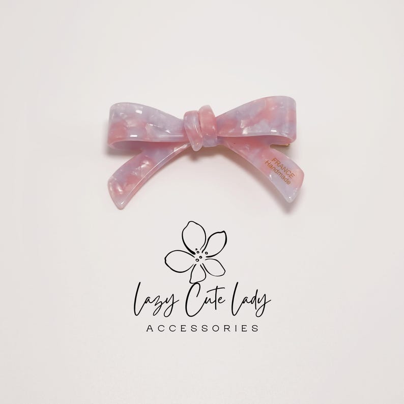 Pu&ograve; includere: Fermaglio per capelli a forma di fiocco marmorizzato rosa chiaro e lilla. Il fiocco &egrave; realizzato in materiale lucido e riporta la scritta "FRANCE Handmade" su una delle code. Il logo "Lazy Cute Lady Accessories" &egrave; sotto.