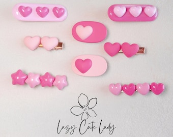 Puede incluir: Un conjunto de pinzas para el pelo en forma de corazón rosa. Las pinzas están hechas de resina y tienen un acabado brillante. Las pinzas están dispuestas en diferentes patrones, incluyendo una fila de tres corazones, una fila de cuatro corazones y un solo corazón. Las pinzas son perfectas para añadir un toque de fantasía a cualquier peinado.