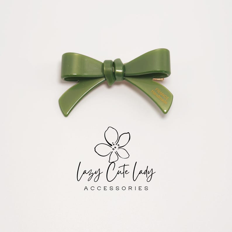 Pu&ograve; includere: Un fermaglio per capelli a forma di fiocco verde con la scritta "FRANCE Handmade" su un lato. Il fermaglio &egrave; realizzato in materiale lucido ed &egrave; posto su uno sfondo bianco. L'immagine include anche il testo "Lazy Cute Lady ACCESSORIES".