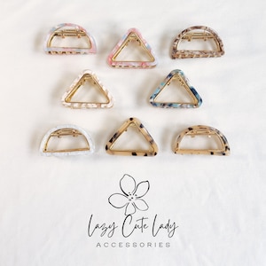 May include: Assortment of hair claw clips in various shapes and patterns. The clips feature gold-toned metal hardware and colorful, marbled designs in pink, blue, brown, and white. The image includes the text "Lazy Cute Lady Accessories".
