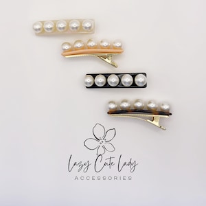May include: Four hair clips with faux pearl accents. The clips are in various colors, including clear, peach, black, and tortoiseshell. The clips have a barrette style clasp. The text "Lazy Cute Lady Accessories" is at the bottom of the image.