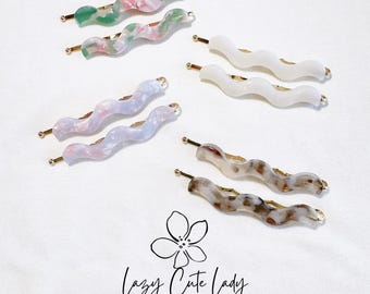 May include: Set of six wavy hair clips in various colors, including pink, green, white, and brown. The clips are made of plastic and have a gold metal bar.