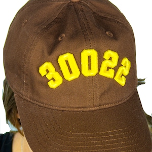 May include: A brown baseball cap with a yellow embroidered "3002" on the front.