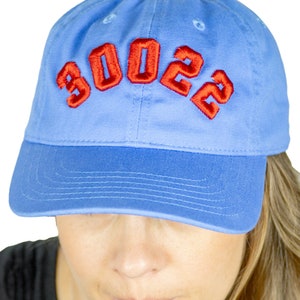 Può includere: Un berretto da baseball blu con un "2023" ricamato in rosso sul davanti.