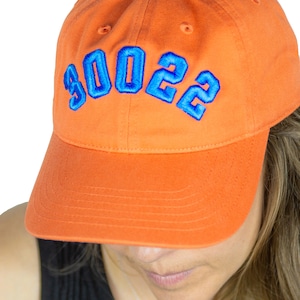Può includere: Un cappello da baseball arancione con un "2022" ricamato in blu sul davanti.