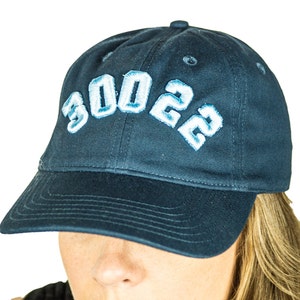 Può includere: Un berretto da baseball blu navy con un "3002" ricamato in bianco sul davanti.
