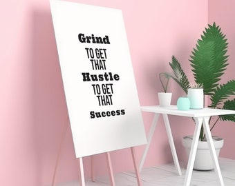 May include: A white poster with black text on an easel. The text reads "Grind to get that Hustle to get that Success". The poster is in front of a pink wall.
