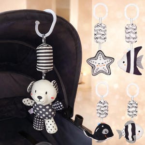 Może przedstawiać: Czarno-biała zabawka do wózka dziecięcego z misiem, rozgwiazdą, rybą i wielorybem. Miś ma grochy i wzory w kratkę. Zabawki wiszą na białym plastikowym haczyku.