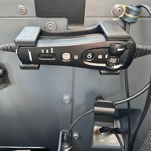May include: A black Bose control module mounted in a plastic holder, featuring a mute switch, Bluetooth button, power button, and volume dial. Cables extend from both sides, with additional audio ports labelled MIC and HOPH visible below.
