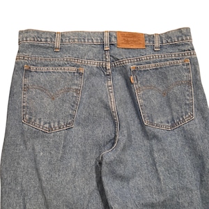 May include: Light blue denim jeans with classic five-pocket styling. Features a brown leather patch with a brand logo on the back waistband. The back pockets have a signature stitch design.