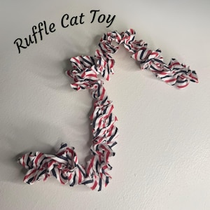 May include: A red, white, and blue striped fabric cat toy with a ruffled texture. The toy is made of soft fabric and is designed to be interactive for cats.