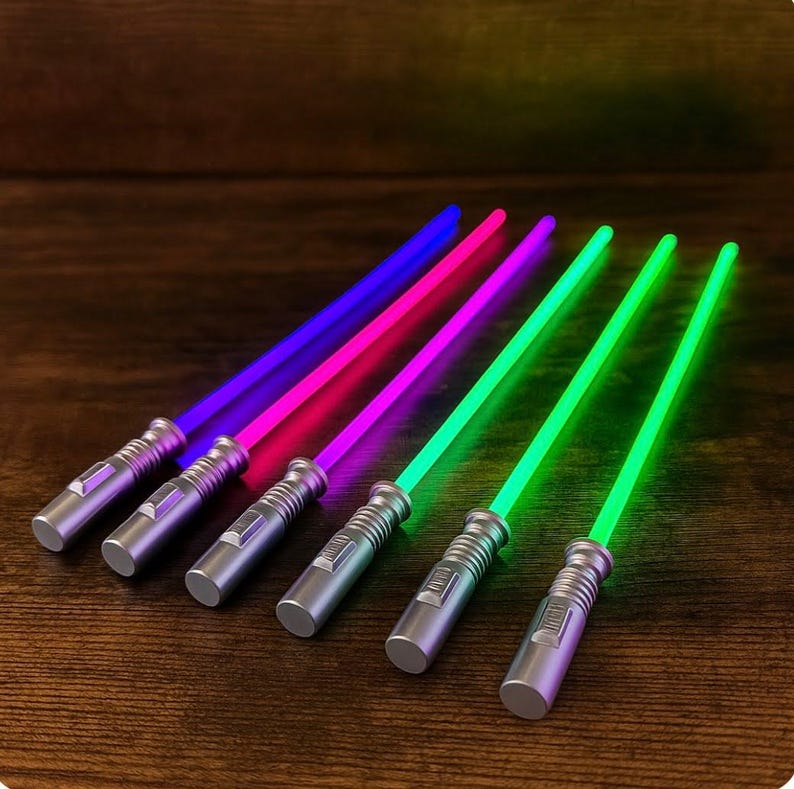 Puede incluir: Seis sables de luz de juguete con hojas brillantes en azul, rosa y verde. Los mangos son plateados con dise&ntilde;os detallados. Los sables de luz est&aacute;n dispuestos diagonalmente sobre una superficie de madera oscura.