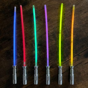 Puede incluir: Seis sables de luz de juguete en azul, rojo, verde, morado, amarillo y naranja. Cada sable tiene un mango plateado y una hoja brillante, ideal para juegos imaginativos y fiestas tem&aacute;ticas.