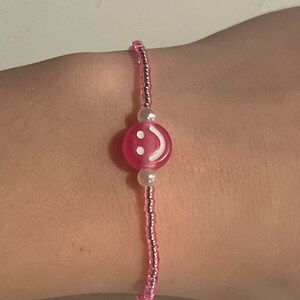 May include: Pink beaded bracelet with a pink smiley face charm and white pearl beads.