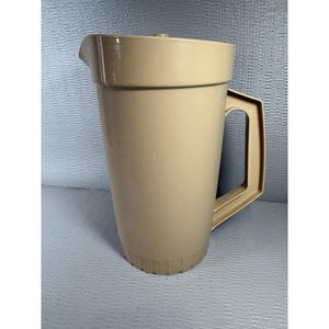 May include: A beige plastic pitcher featuring a tapered cylindrical body, a wide pouring spout, and a sturdy angular handle. The base of the pitcher is decorated with a series of vertical ridges, and the top includes a matching fitted lid.
