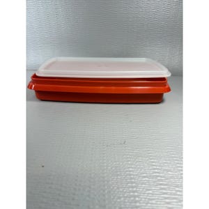 May include: A stack of two rectangular food storage containers. The bottom container is a vibrant orange, and the top container has a white lid. The containers are made of plastic and are designed for food storage.