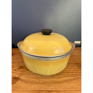 May include: A round yellow cooking pot with a matching domed lid and a black knob handle. The pot features a silver-toned metal rim around the top edge, contrasting with the smooth, solid yellow finish of the body and lid.