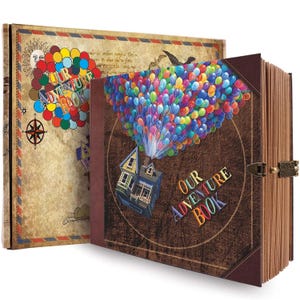 Puede incluir: Un libro marrón de tapa dura "Our Adventure Book" con un gráfico colorido de globos y una casa. El libro tiene un cierre de metal y una cubierta de estilo vintage con una brújula y un diseño de sol. El título está en letras coloridas.
