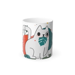 Puede incluir: Taza de cerámica blanca con una ilustración de dibujos animados de un gato blanco con una hoja verde en la boca y un monóculo. El gato está rodeado de formas abstractas de colores.