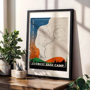 May include: A framed Everest Base Camp map print. The print features a detailed map with a route marked in black, set against a backdrop of orange, blue, and green. Text includes "100 MILES / 160 KM" and "EVEREST BASE CAMP". The frame is black.