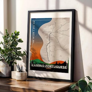 May include: Framed art print of the Camino Portuguese route, with a map design. The print features a color scheme of blue, orange, and green, with the text "168 miles / 270 km" and "Camino Portuguese Europe". The artwork is displayed on a wooden surface.