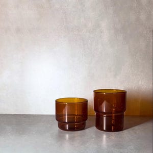 May include: Two amber glass tumblers, one taller than the other, with a rounded bottom and a slightly flared top.