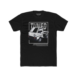 May include: Black t-shirt with a white graphic of a small white pickup truck with the word "TUNED" in a white box above it. The text below the truck reads "These little pickups were not built to truck the heaviest loads or to go middle-over-80 MPH, but they have captured the hearts of millions, earned two credits for American highways. These imports must work hard to gain respect, but they do, and they do it with style."