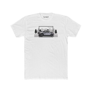 May include: White t-shirt featuring a graphic of a gray pickup truck with the word "Tuned" above and inside a rectangular frame. The word "tuned" is also printed on the upper center of the shirt.