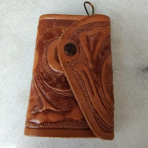 May include: A brown leather key chain with a decorative embossed pattern. The key chain has a metal loop for attaching keys.