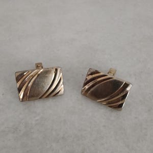 May include: A pair of gold-toned cufflinks with a wavy, textured design.