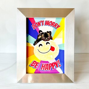 May include: A framed print with a colorful background and a pug dog sitting on a yellow smiley face. The text "Don't Worry Be Happy!" is printed in bold letters.