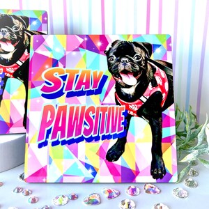 Może przedstawiać: Kwadratowa ceramiczna podkładka z kolorowym geometrycznym wzorem i czarnym mopse, kt&oacute;ry nosi czerwoną szelkę. Tekst "STAY PAWSITIVE" jest napisany w kolorach tęczy.