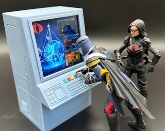 May include: A light blue computer console with a screen displaying a world map and Cobra logo, operated by a blue-armored figure with a cape. A black-clad figure with glasses stands nearby. Both figures feature red Cobra emblems on their chests.