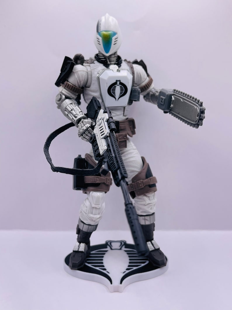 Peut inclure: Une figurine d'action blanche tenant un fusil noir et argent, une cha&icirc;ne noire et argent et une tron&ccedil;onneuse noire et argent. La figurine porte un casque blanc avec une visi&egrave;re bleue et un costume blanc et noir. La figurine est debout sur une base blanche avec un logo Cobra noir.