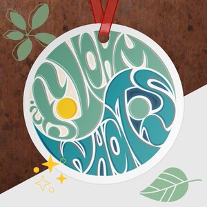 May include: Circular ornament with a teal and blue yin-yang design, featuring a yellow sun-like shape. The ornament has a red ribbon for hanging. Decorative stars and a leaf are in the background. The design is on a white background.