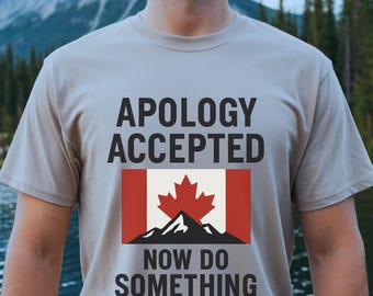 Puede incluir: Una camiseta gris con el texto "Apology Accepted" y una bandera canadiense con una cordillera debajo. El texto "Now Do Something" está debajo de la bandera.