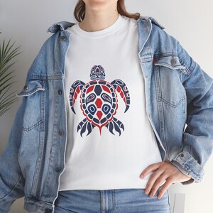 Peut inclure: T-shirt blanc avec un motif de tortue stylisé bleu et rouge. La tortue a un motif géométrique et fait face à l'avant.