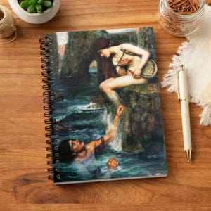 May include: Spiral-bound notebook with a classical painting of a mermaid with a lyre and a person in the water. The artwork depicts a dramatic scene with a rocky background and flowing water. The notebook has a black spiral binding.