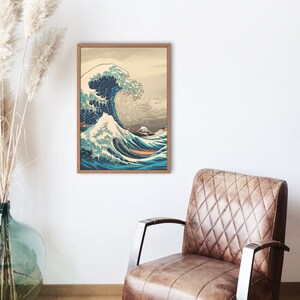 Op de afbeelding: Een ingelijste print van een Japanse houtsnede die een grote golf toont die tegen een berg aanbreekt. De golf is blauw en wit, en de berg is grijs. De print is ingelijst in een lichtbruin houten lijst.