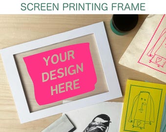 May include: A white screen printing frame with a pink insert that reads "YOUR DESIGN HERE." The image also shows printed artwork, ink, and a canvas bag with a printed design. The text "SCREEN PRINTING FRAME" is at the top.