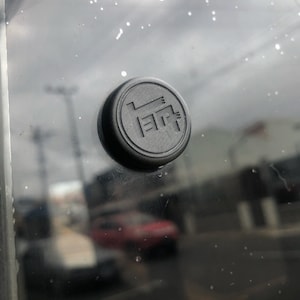 Könnte beinhalten: Ein schwarzer Plastikknopf mit den Buchstaben "E.R." in Prägung.