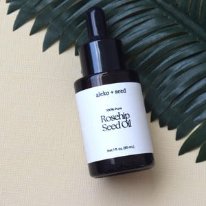 May include: A glass bottle with a black dropper top and a white label. The label says "aleko + seed 100% Pure Rosehip Seed Oil Net 1 fl. oz. (30 ml)"