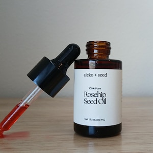 Rosehip Seed Oil in amber glass bottle by aleko and seed. Dropper top bottle with pure, organic rosehip seed oil, Rosa canina resting on the bottle