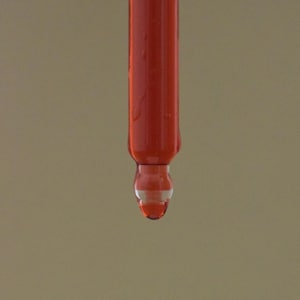 May include: A close-up of a red liquid dripping from a glass dropper.